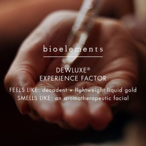 Hand receiving drops of Dewluxe body oil with text overlay describing the experience: 'Feels like decadent + lightweight liquid gold, smells like an aromatherapeutic facial.'