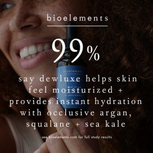 Smiling woman holding Dewluxe bottle with text overlay: '99% say Dewluxe helps skin feel moisturized + provides instant hydration with occlusive argan, squalane + sea kale.'