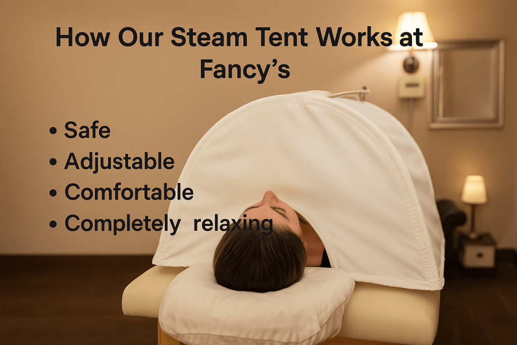 A woman lies on a massage table with her head exposed from a spa steam tent. On the left, overlaid text reads: "How Our Steam Tent Works at Fancy’s" with bullet points: Safe, Adjustable, Comfortable, Completely relaxing — all set in a cozy, softly lit spa room.